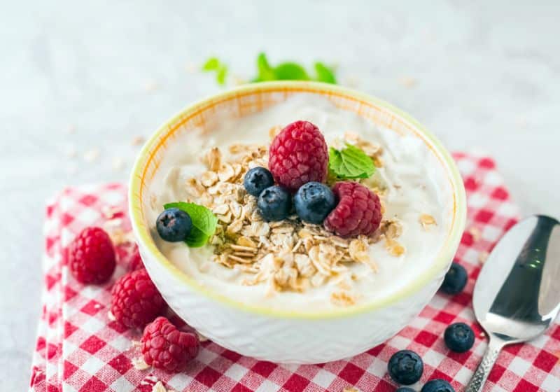 Frutas com iogurte e aveia potinho em uma mesa com iogurte e mirtilos e framboesa e uma colher do lado