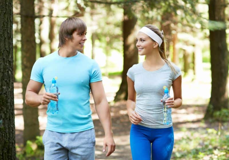 um homem e uma mulher com um garrafinha na mão caminhando em uma floresta 