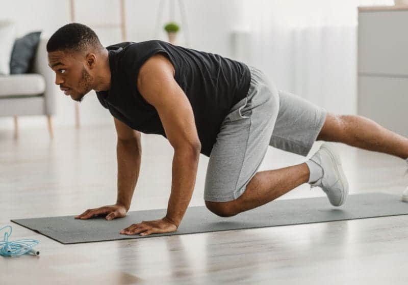 Corrida Estacionária homem com um joelho no chão e a outra perna esticada e as mão no chão com um fundo branco