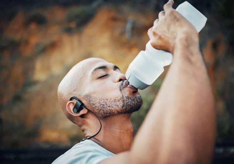 homem bebendo água e com um fone no ouvido 