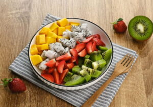 potinho com salada de fruta e um guardanapo embaixo e talheres do lado com morango em uma mesa