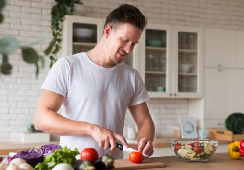 alimentação saudável homem em uma cozinha cortando tomate em uma tabua de madeira
