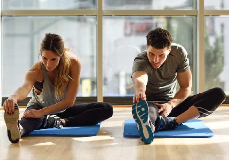 homem e mulher fazendo alongamento no tapete de exercício 