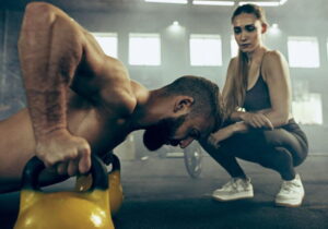 mulher olhando homem a fazer flexão com peso, em uma academia