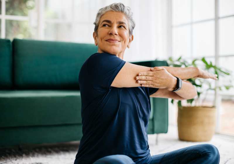 Uma senhora se alongando em uma sala de casa