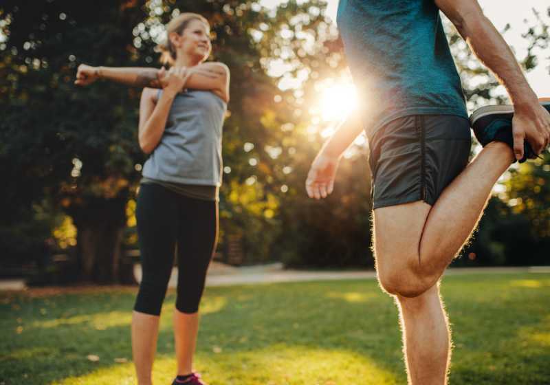 Casal se alongando para realizar uma caminhada em um parque