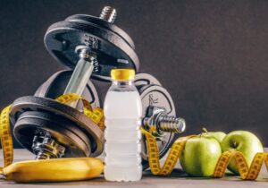 Imagem com aparelhos de musculação, frutas e uma garrafa de água