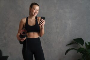 Mulher com um tapete na mão e mexendo no celular com a outra mão