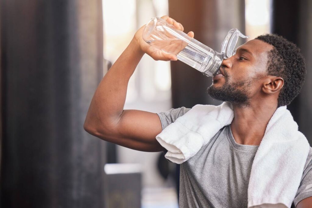 Homem bebendo água em garrafa transparente e com toalha no pescoço