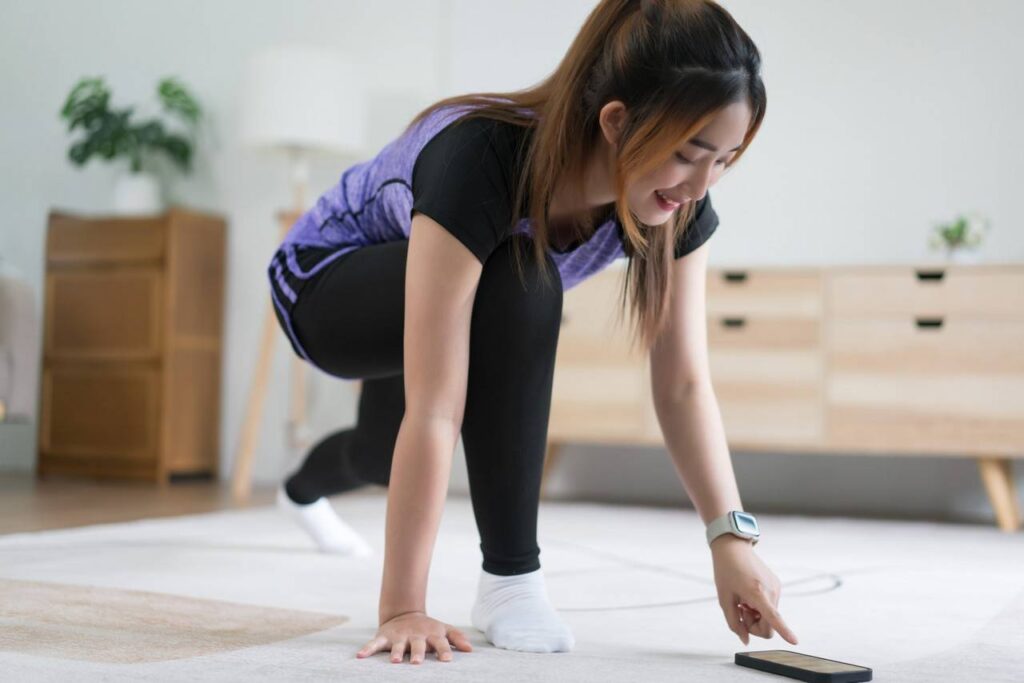 Mulher realizando o exercício chamado avanço, e tocando com uma das mão so celular no chão.