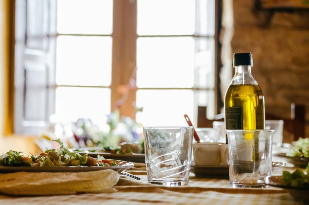 Garrafa de azeite de oliva em mesa, com copos e pratos