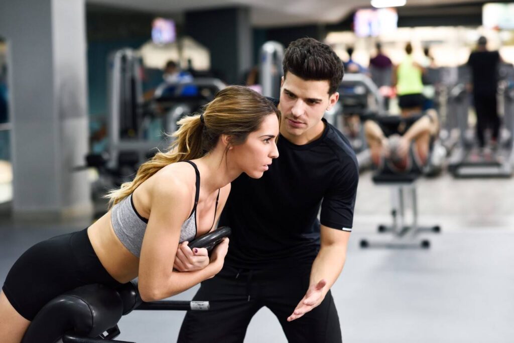 personal trainer orientando aluna a executar exercício em academia