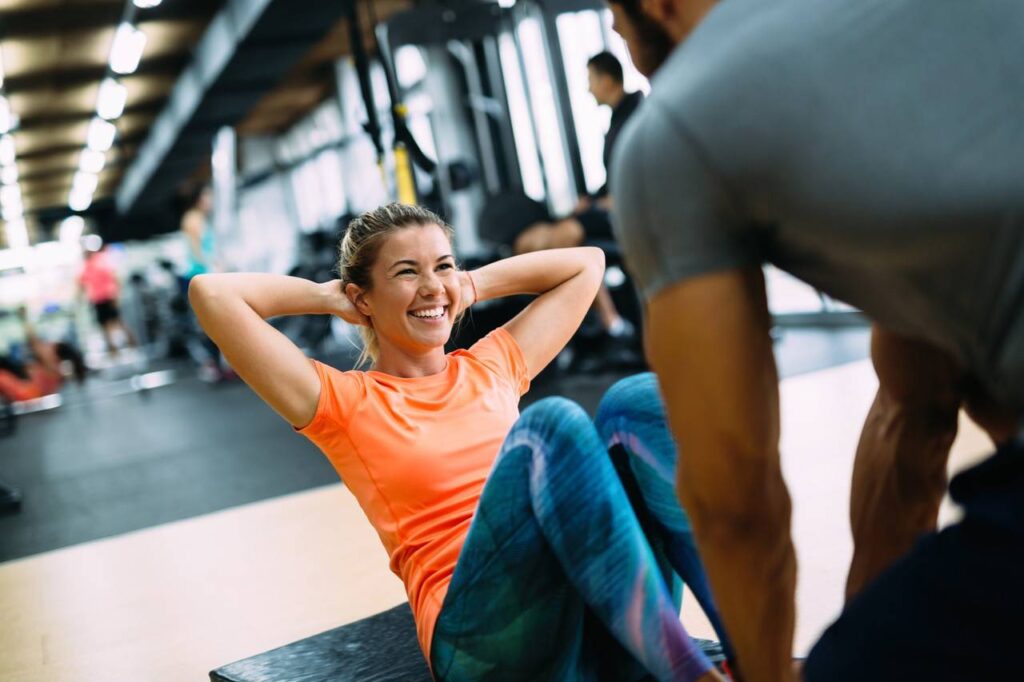 Personal trainer segurando pés de aluna para que ela possa fazer exercício abdominal