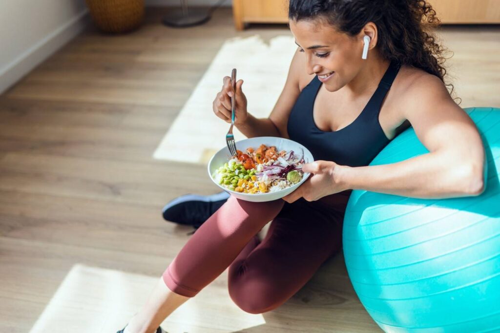 Mulher sentada ao chão segurando um prato de comida com legumes e salada