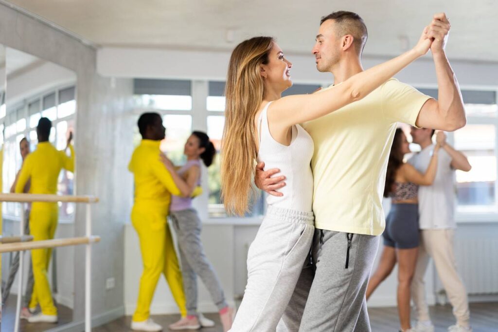 Casal praticando dança, ao fundo mais dois casais também dançando