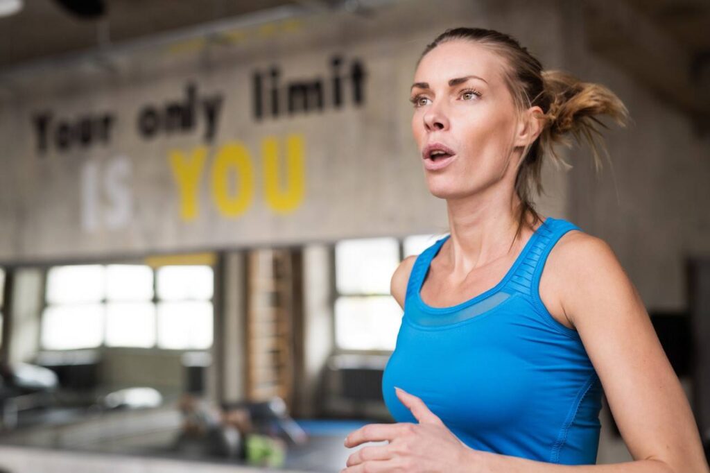 Mulher praticando exercícios físicos de blusa azul, ao fundo academia