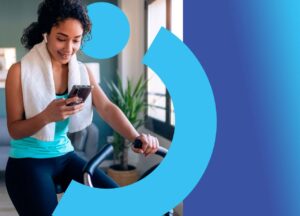 Mulher em bicicleta ergométrica pedalando e olhando o celular em mãos